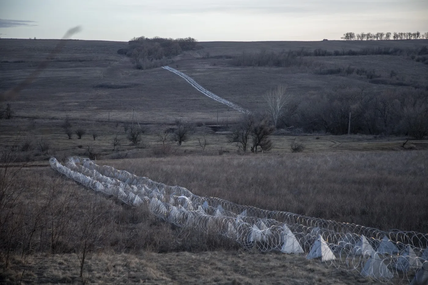 Peisaj rural din Donbas, cu sârma ghimpată și câmpuri întinse.