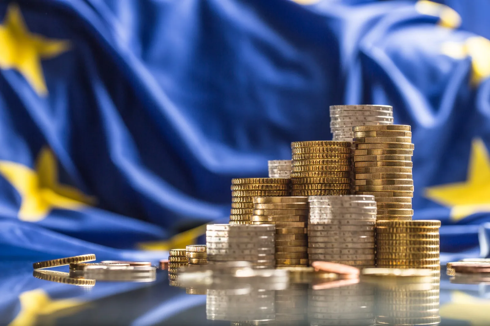 Monede aranjate pe un fundal cu steagul Uniunii Europene.