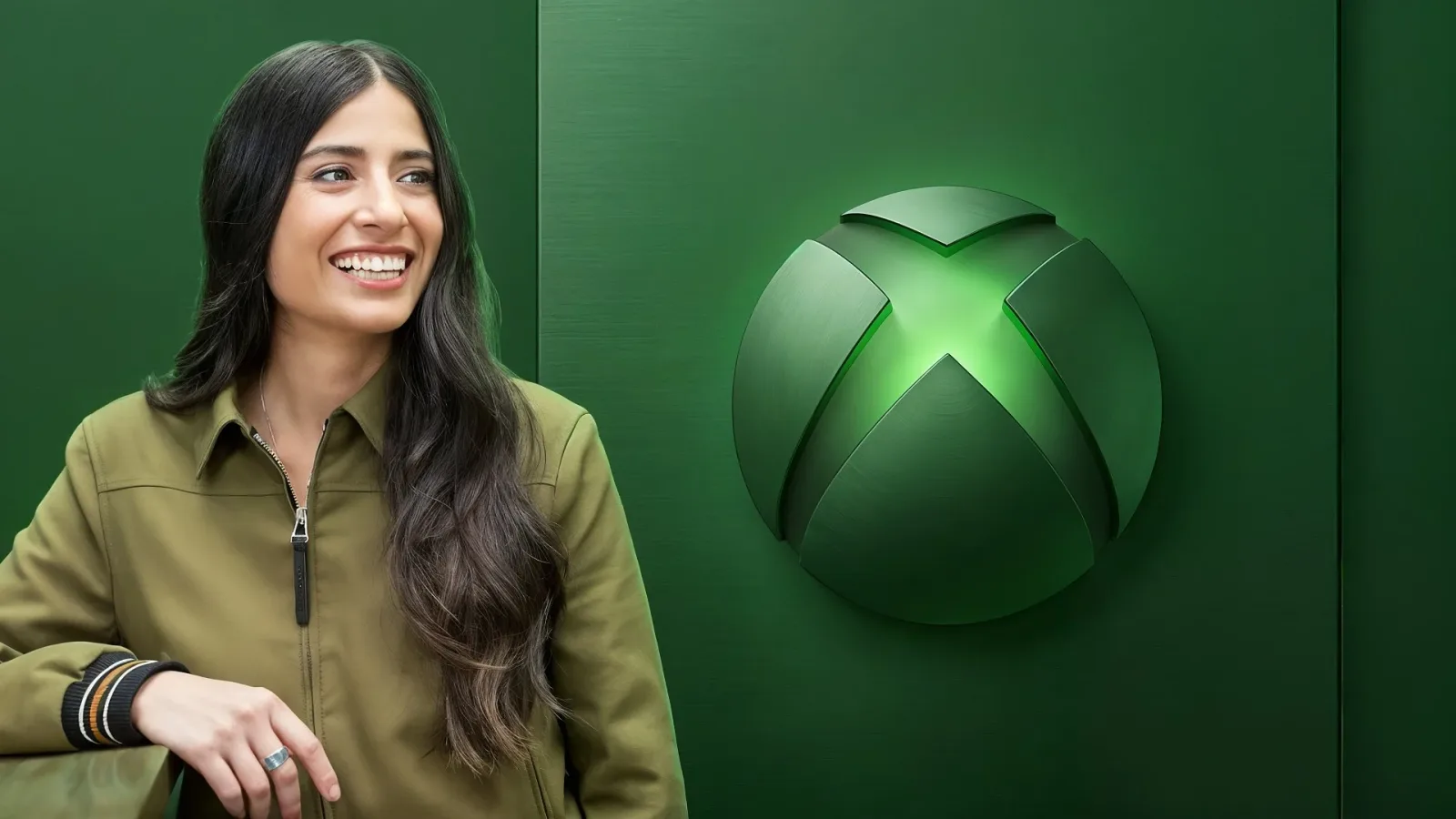 Asha Sharma zâmbește în fața logo-ului Xbox, simbolizând schimbări în companie.