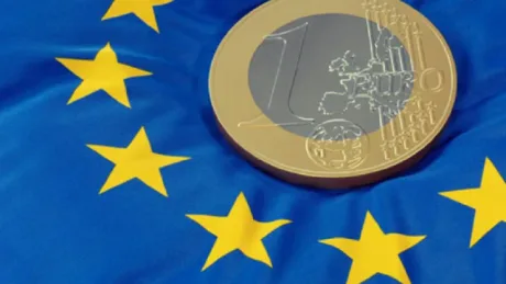 Monedă euro pe fundal cu steagul Uniunii Europene.