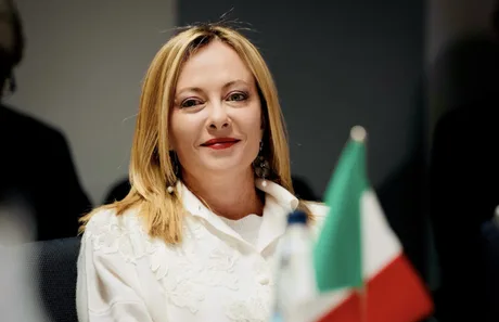 Giorgia Meloni la o întâlnire oficială, zâmbind și purtând o bluză albă.