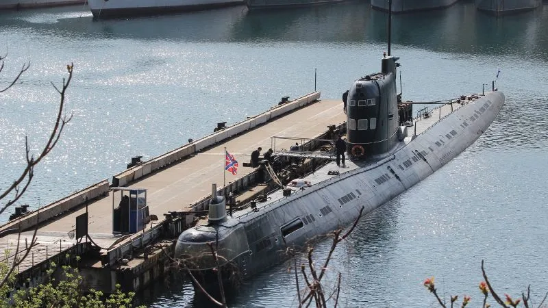Submarin ancorat în port, reflectându-se în apă liniștită.