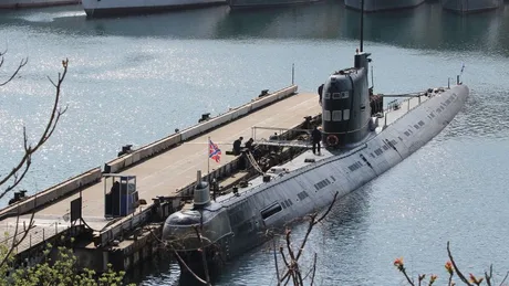 Submarin ancorat în port, reflectându-se în apă liniștită.