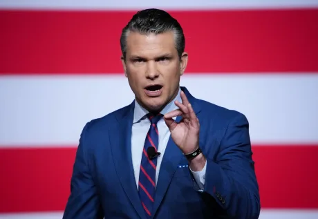Pete Hegseth discutând despre investiții în apărare pe fundalul steagului american.