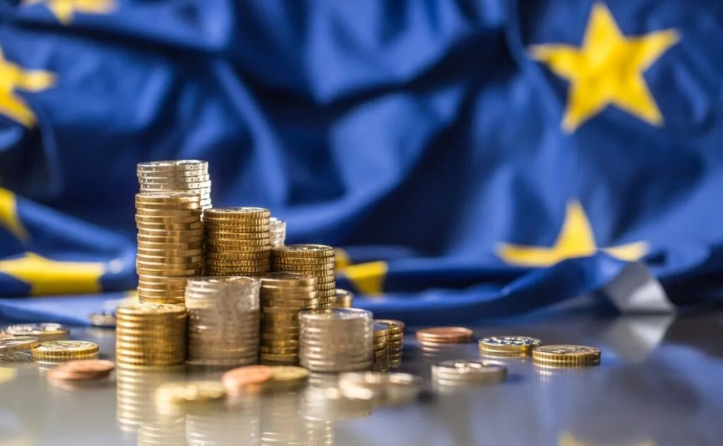 Monede pe un fundal cu steagul Uniunii Europene, simbolizând adoptarea euro.