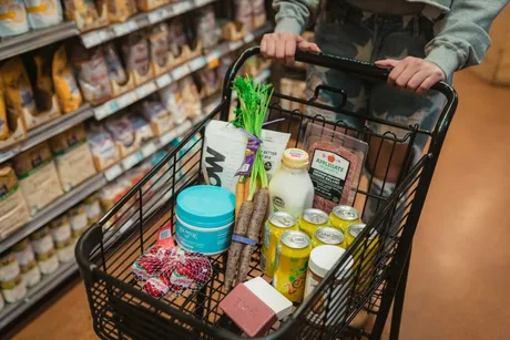 Coș de cumpărături plin cu alimente variate în supermarket.
