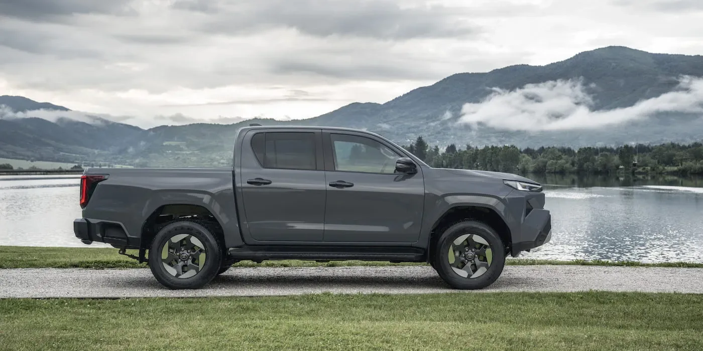 Pickup-ul electric Hilux BEV pe malul unui lac, cu munți în fundal.