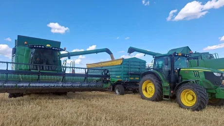Recoltarea orzului cu utilaje agricole în câmp, sub un cer senin.