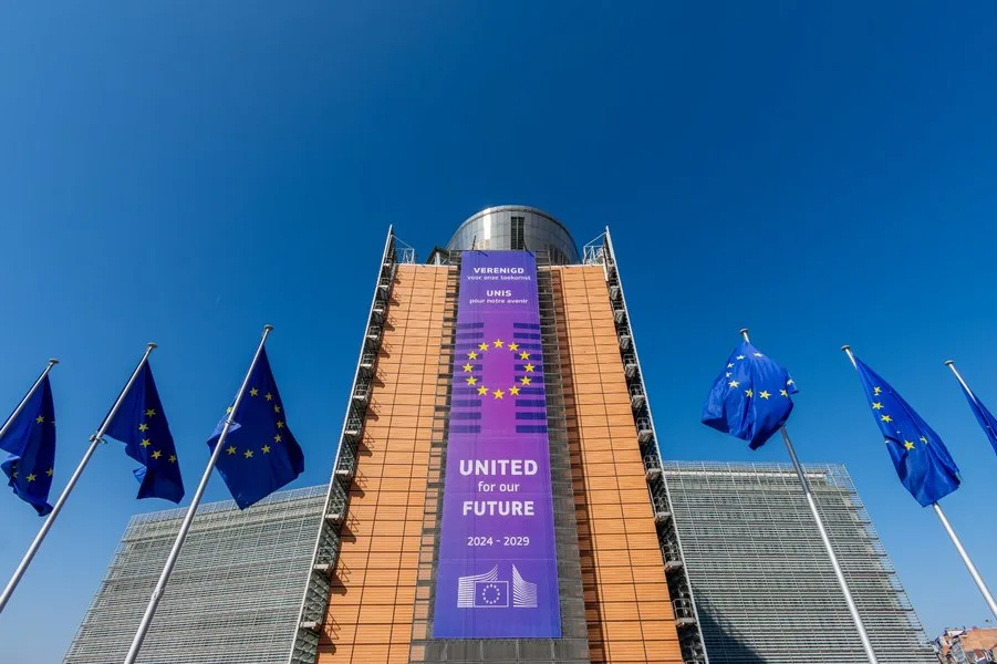 Sediul Comisiei Europene cu steaguri în față și cer senin.