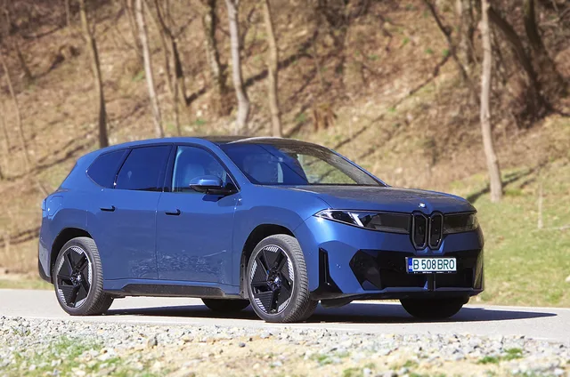 Un SUV BMW parcurs pe un drum de țară, înconjurat de natură.