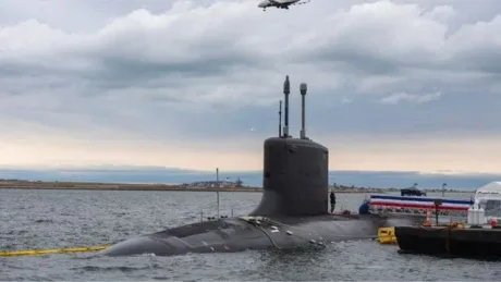 Submarin în apă, cu un elicopter deasupra, pe un fundal de nori.