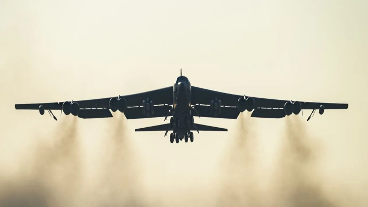 Bombardier B-52H în zbor, cu fum de motor vizibil în spate.