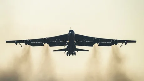 Bombardier B-52H în zbor, cu fum de motor vizibil în spate.