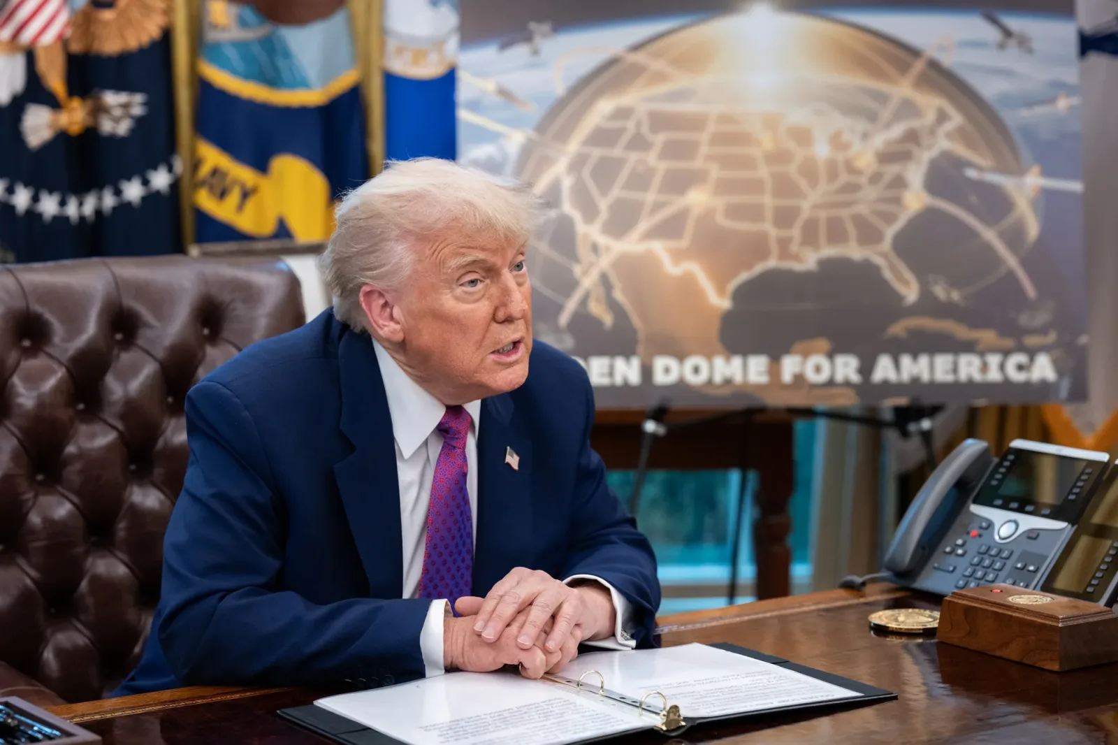 Donald Trump discutând la biroul său, cu harta Americii în fundal.
