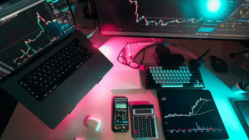 Birou modern cu laptop, monitor și instrumente financiare.