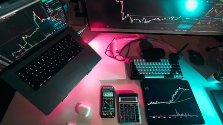 Birou modern cu laptop, monitor și instrumente financiare.