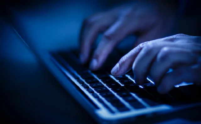 Utilizator lucrând pe laptop într-un mediu întunecat, concentrat pe securitate cibernetică.