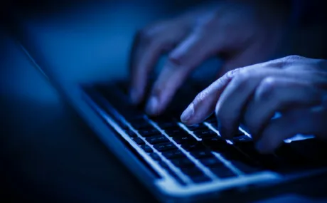 Utilizator lucrând pe laptop într-un mediu întunecat, concentrat pe securitate cibernetică.