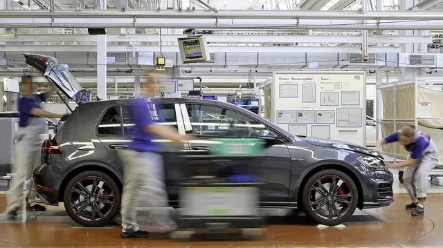 Angajați lucrând într-o fabrică Volkswagen, cu un autoturism pe linia de producție.