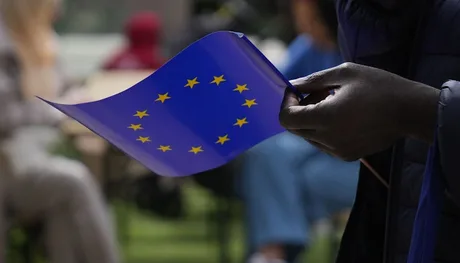 Un bărbat ține o steag al Uniunii Europene în timp ce discută despre comerț.
