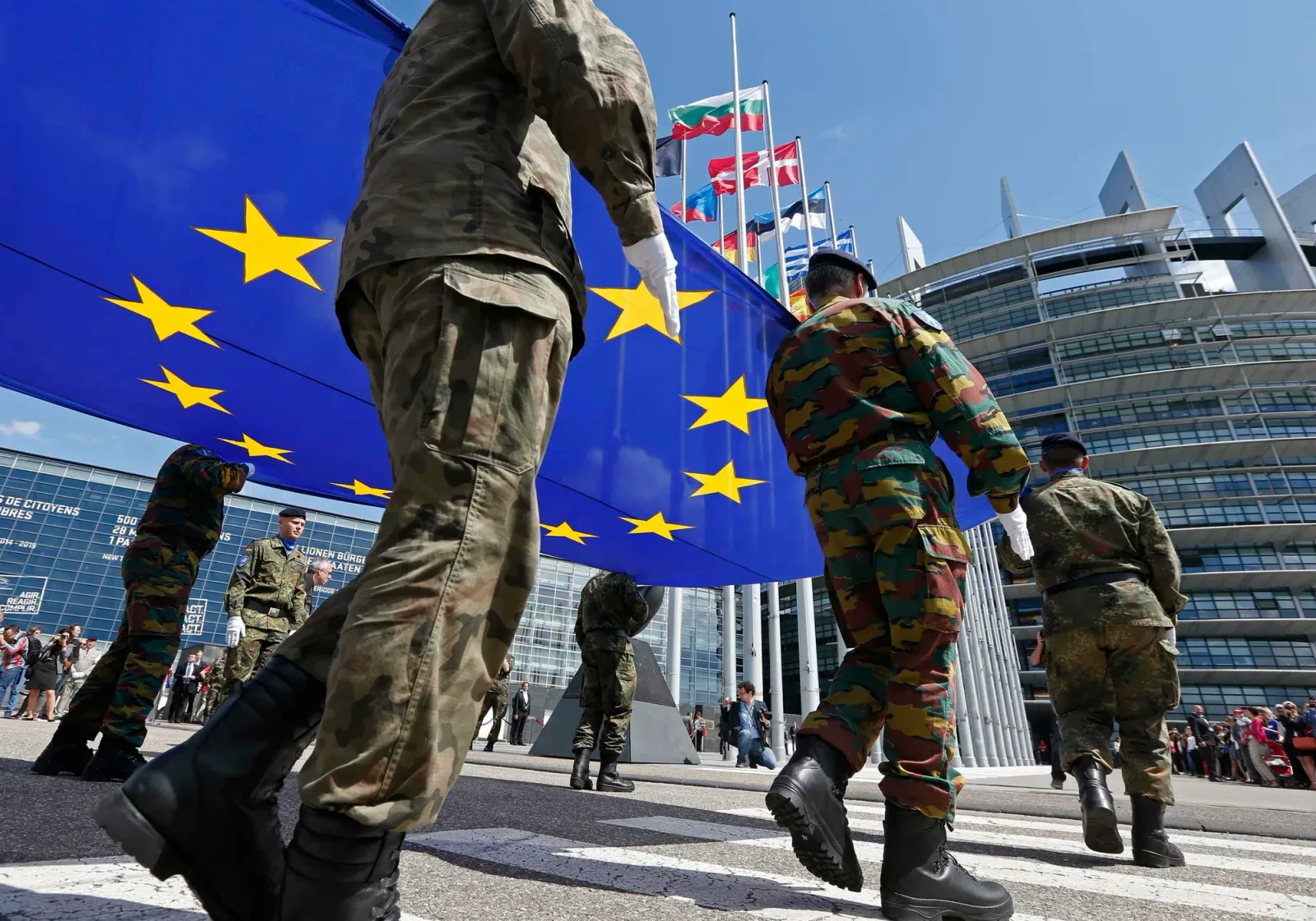 Soldați defilând cu steagul Uniunii Europene în fața clădirii Parlamentului European.