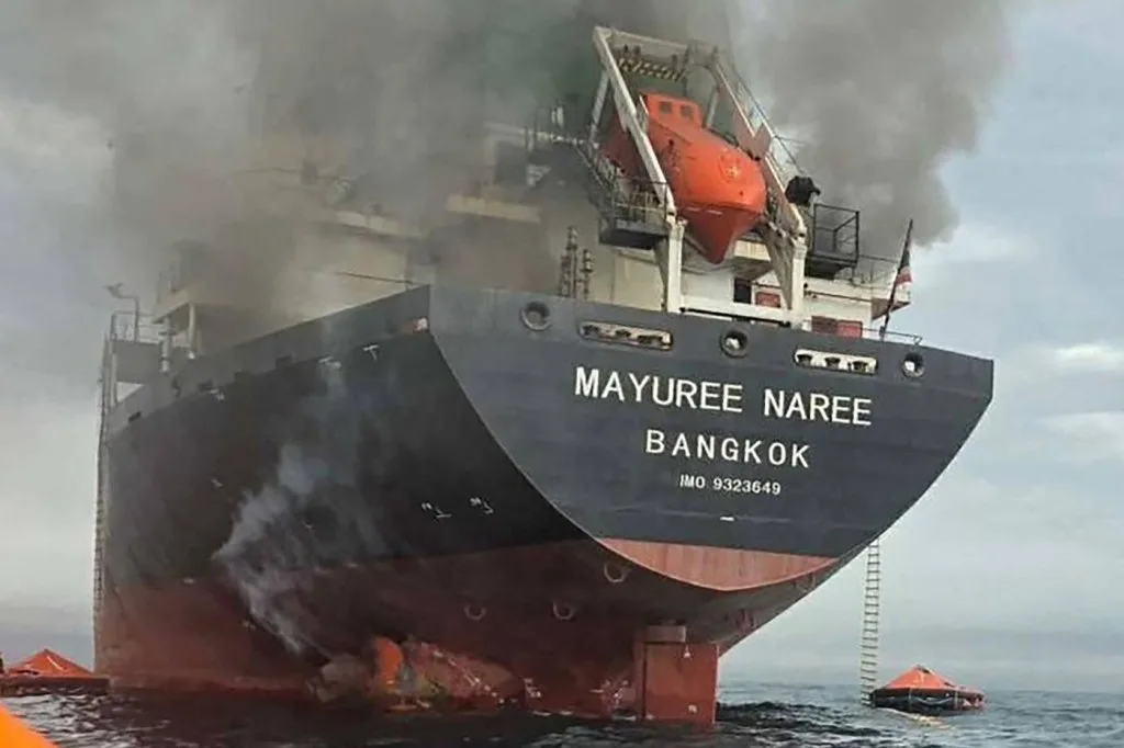 Nava în flăcări pe mare, cu echipaje de salvare în acțiune.