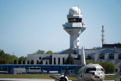 Turn de control aerian cu un avion parcat în față, pe un fundal senin.
