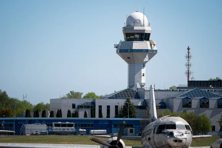 Turn de control aerian cu un avion parcat în față, pe un fundal senin.