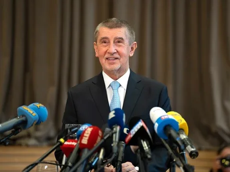 Andrej Babiš zâmbind în fața presei, înconjurat de microfoane.