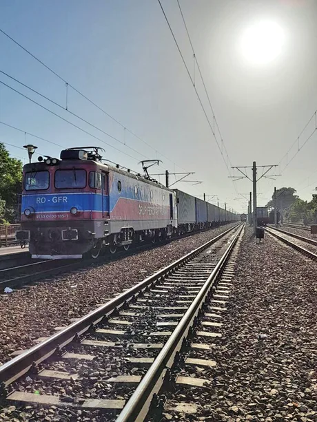 Locomotivă pe calea ferată, transportând vagoane de marfă în soare.