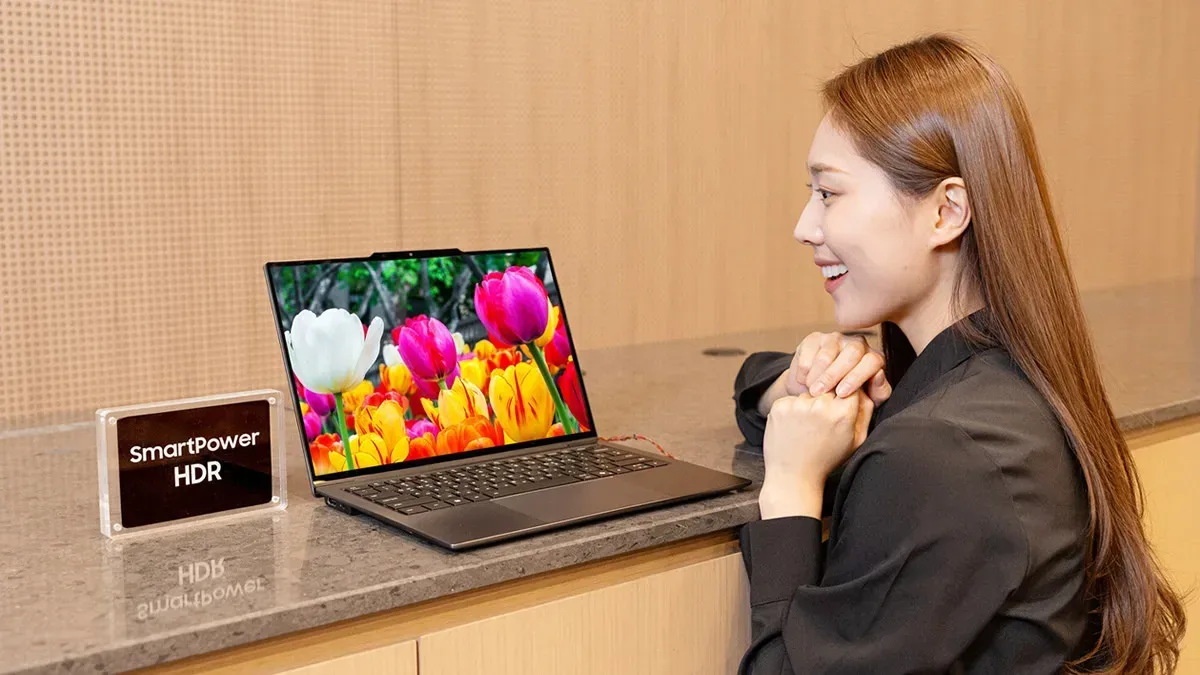 Femeie zâmbitoare lângă laptop cu tehnologia SmartPower HDR activată
