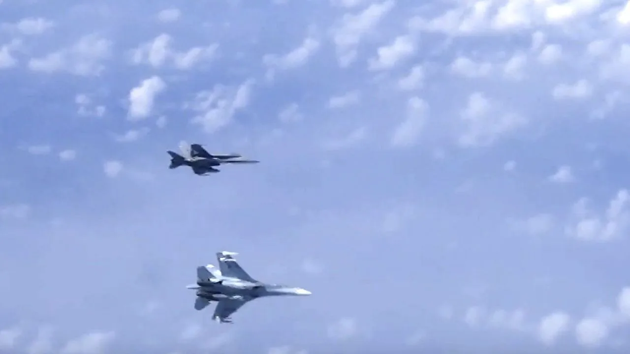 Două aeronave militare zburând în cer, cu nori albi în fundal.
