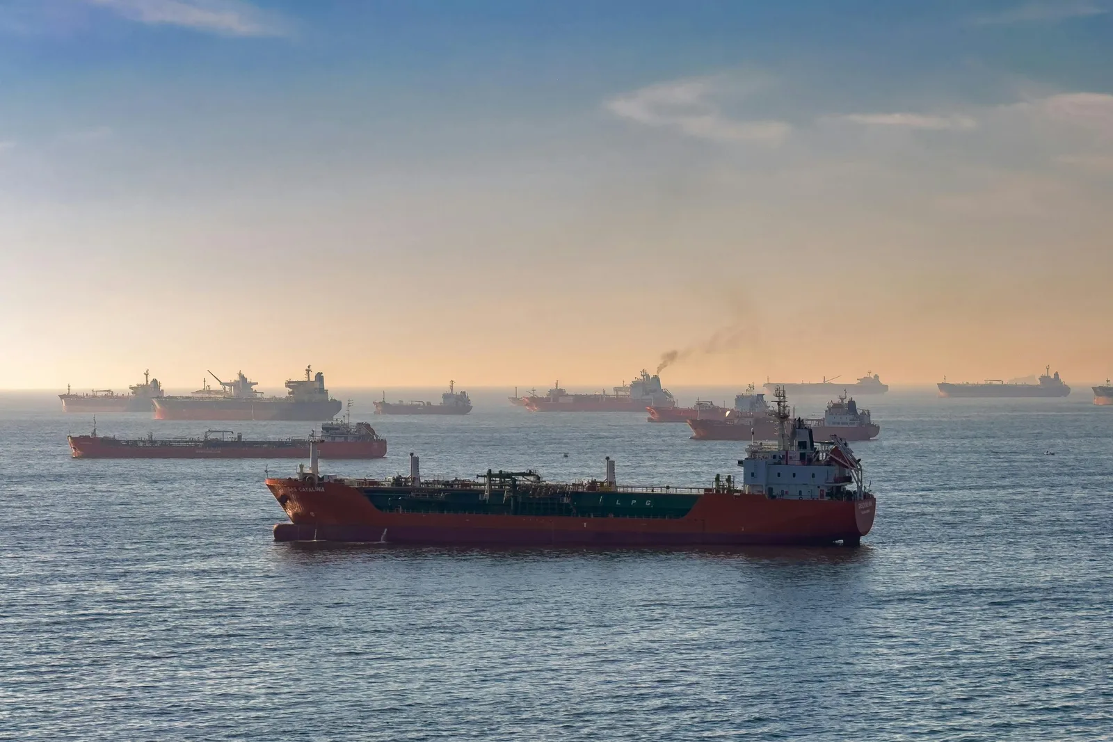 Vas de transport maritim pe fundalul unei mări agitate, cu nave ancorate.