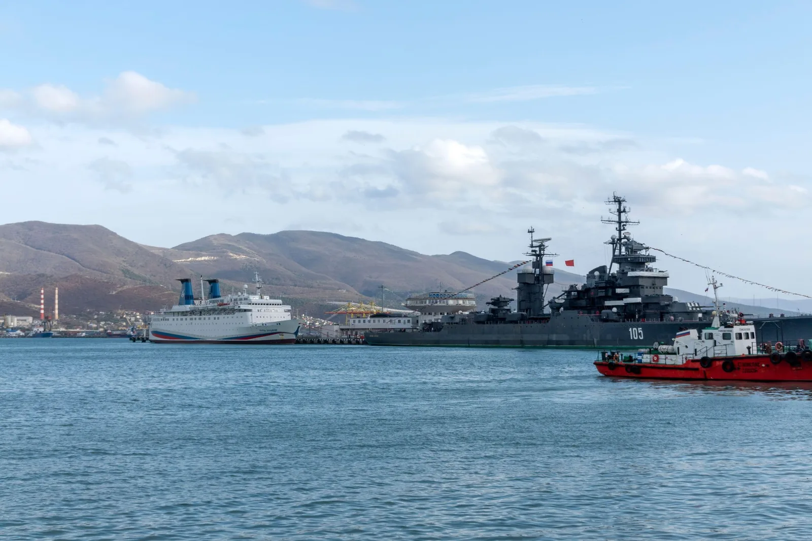 Nava rusă Izumrud ancorată în port, în fundal munți și cer senin.