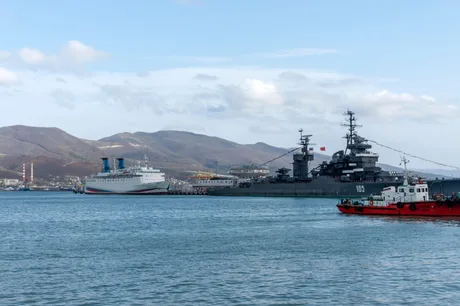 Nava rusă Izumrud ancorată în port, în fundal munți și cer senin.