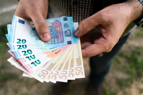 Bărbat ținând bancnote euro în mâini, simbolizând subvențiile agricole.
