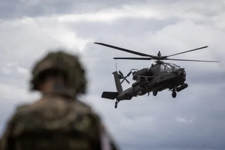 Elicopter militar în zbor, cu soldat observându-l de la sol.