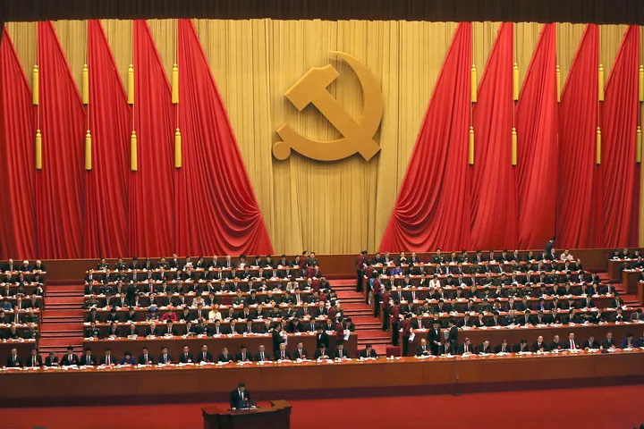 Sesiune oficială a Partidului Comunist în China, cu decor roșu și simboluri emblematice.