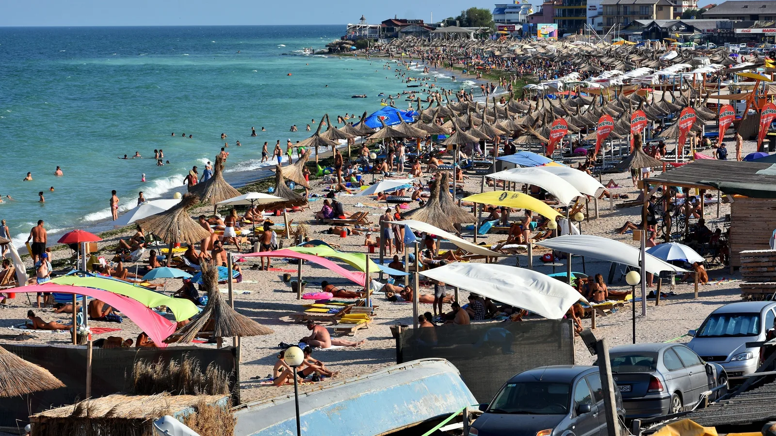 Plajă aglomerată pe litoralul românesc, cu umbrele colorate și turiști relaxați.
