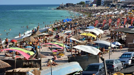 Plajă aglomerată pe litoralul românesc, cu umbrele colorate și turiști relaxați.