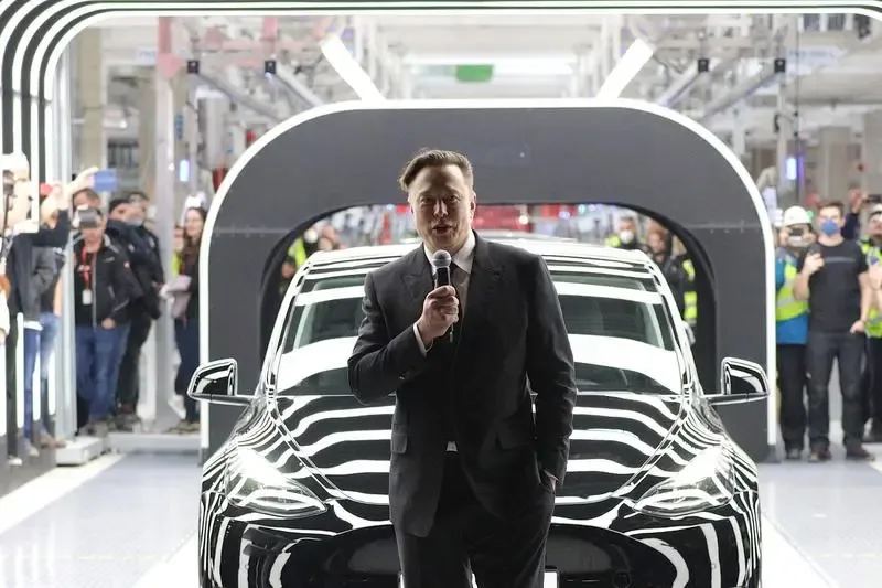 Elon Musk discutând despre viitorul Tesla în fața unei mașini electrice.