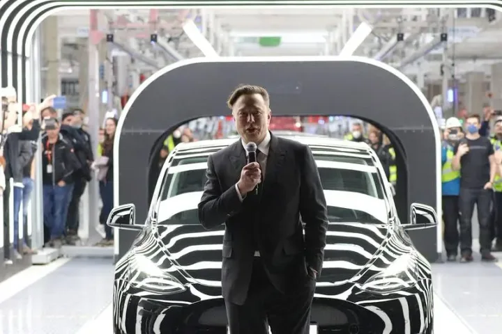 Elon Musk discutând despre viitorul Tesla în fața unei mașini electrice.