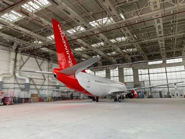 Avion parcat într-un hangar mare, cu lumina naturală intrând prin feronerie.