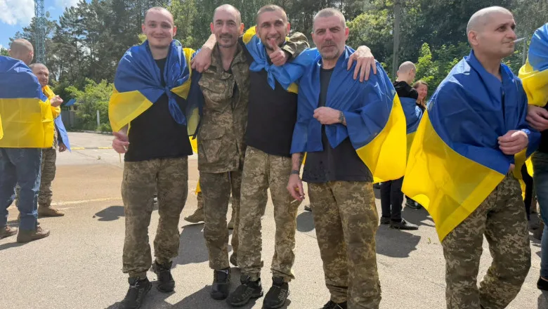 Patru bărbați îmbrăcați în uniformă, zâmbind și ținând steaguri ucrainene.