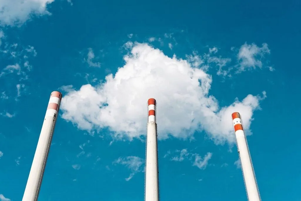 Fumigenele unei centrale electrice pe un fundal albastru cu nori pufoși.