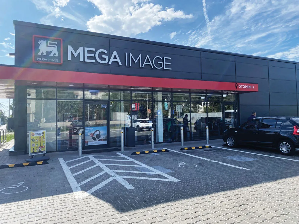 Fațada unui supermarket Mega Image, cu parcarea și clienți la intrare.