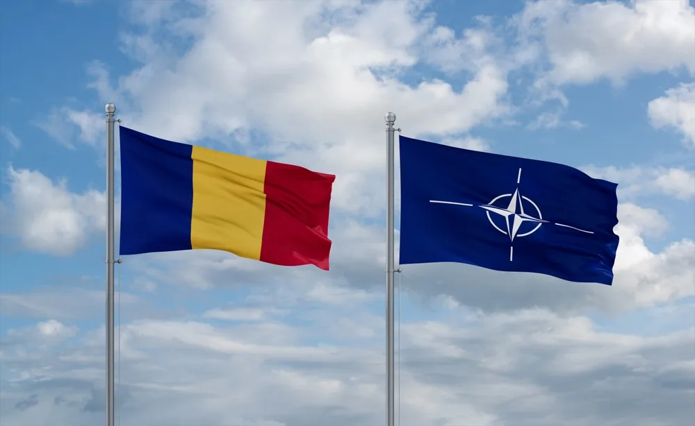 Steagurile României și NATO fluturând împreună sub un cer senin.