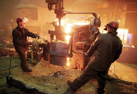 Doi muncitori în fabrică, lucrând cu metal topit.