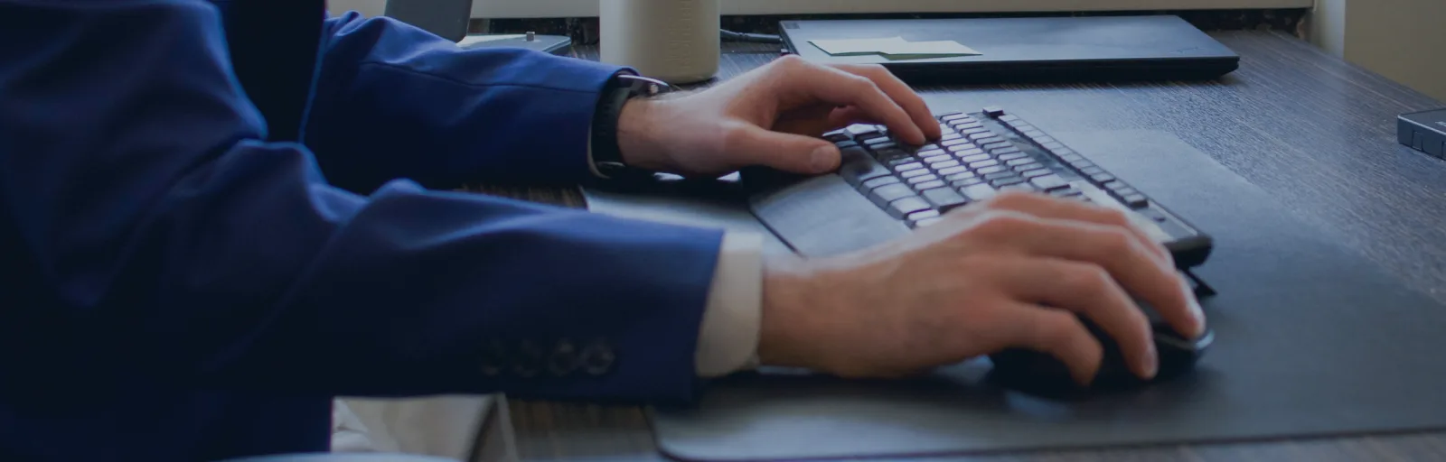 Persoană lucrând la un birou, tastând pe un keyboard.