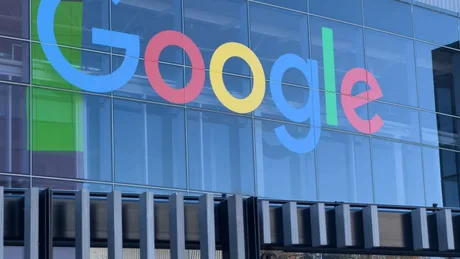 Logo-ul Google pe o clădire modernă, reflectând cerul albastru.